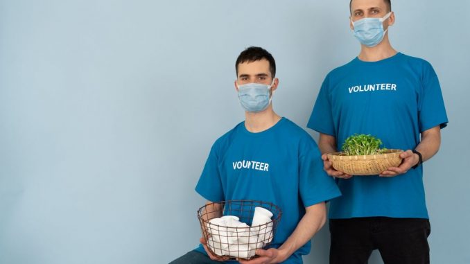 Two volunteers wearing masks holding supplies and plants, promoting charity and environmental protection.