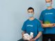Two volunteers wearing masks holding supplies and plants, promoting charity and environmental protection.