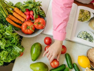 Top view of fresh vegetables and hands arranging them with a recipe book, promoting healthy eating.